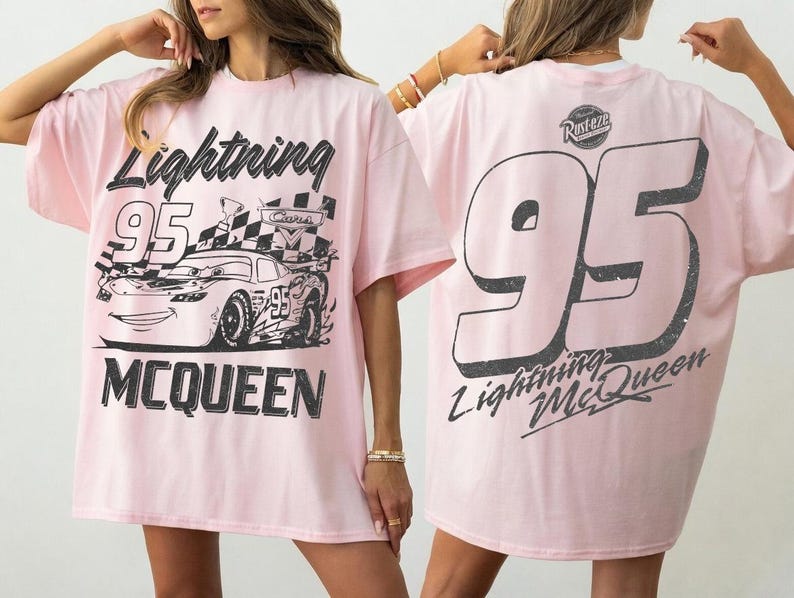 May include: Light pink t-shirt featuring a graphic of Lightning McQueen race car with the number 95. The front of the shirt displays the car and the words "Lightning McQueen". The back of the shirt has a large number 95 and the words "Lightning McQueen".