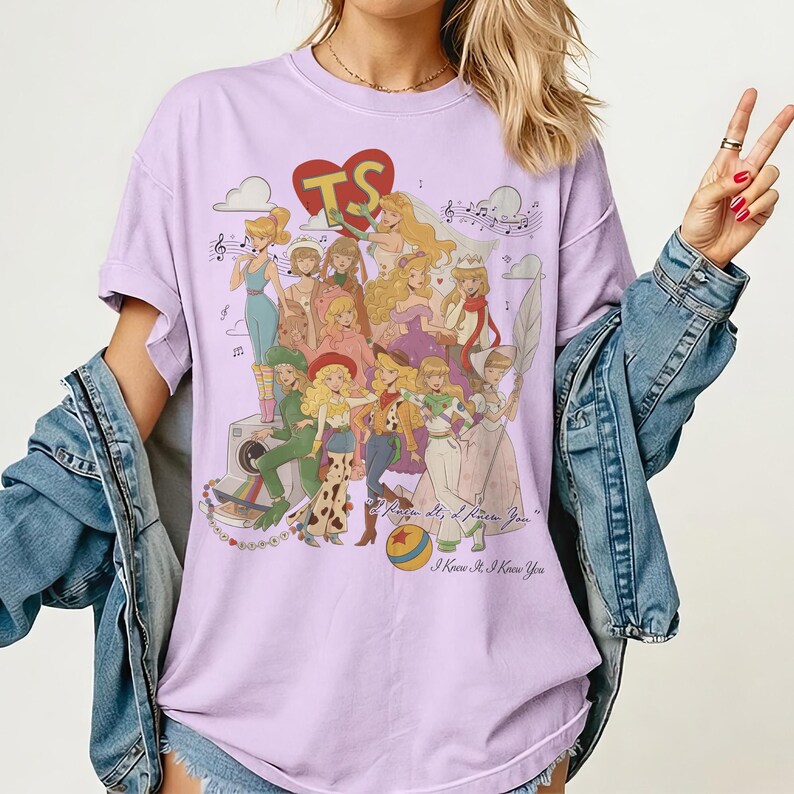May include: A light purple short-sleeve t-shirt featuring a graphic print of various animated characters in different outfits, a red heart with the letters TS, musical notes, a camera, and the text I Knew It, I Knew You printed on the front.