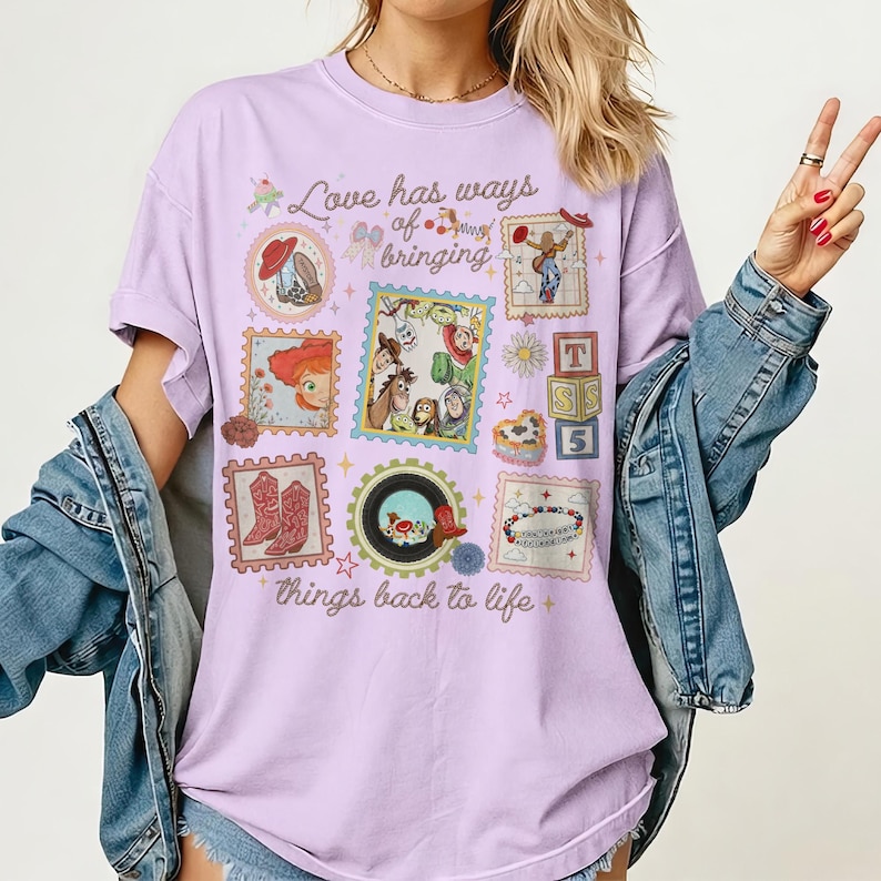 May include: A light purple short-sleeve t-shirt featuring a collage of Toy Story character graphics and stamps. The text reads, Love has ways of bringing things back to life. The design includes illustrations of Woody, Buzz, Jessie, and other characters.