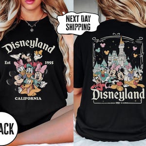 May include: Black t-shirt featuring a Disneyland graphic with Mickey Mouse, Minnie Mouse, Donald Duck, Daisy Duck, Goofy, and Pluto. The front of the shirt says "Disneyland Est 1955 California". The back of the shirt has a Disneyland castle graphic.
