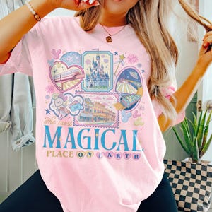 May include: Pink t-shirt with a colorful graphic featuring various theme park attractions and the text "The most MAGICAL PLACE ON EARTH". The design includes a castle, train, and other park elements.