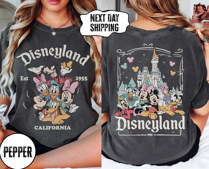 May include: Dark gray t-shirt featuring the Disneyland logo with Mickey Mouse, Minnie Mouse, Donald Duck, Daisy Duck, and Goofy. The front of the shirt has the Disneyland logo and the text "Est 1955 California". The back of the shirt has a castle and the Disneyland logo.