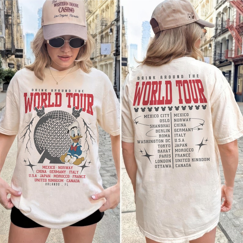 May include: Cream-colored t-shirt with "DRINK AROUND THE WORLD TOUR" in red text. The front features a graphic of a globe and Donald Duck. The back lists cities like Mexico City, Oslo, and Shanghai.
