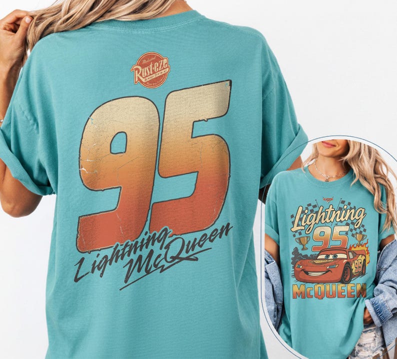 K&ouml;nnte beinhalten: T&uuml;rkisfarbenes T-Shirt mit einer gro&szlig;en 95 in Orange und Gelb, und dem Text "Lightning McQueen". Das Shirt hat auch ein "Rust-eze"-Logo auf dem oberen R&uuml;cken und eine Grafik von Lightning McQueen auf der Vorderseite.