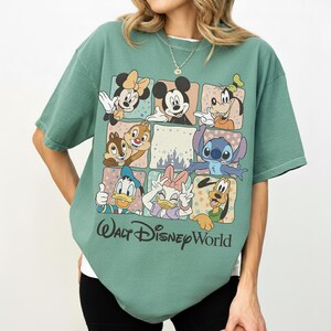 K&ouml;nnte beinhalten: Gr&uuml;nes T-Shirt mit einem Rasterdesign, das Disney-Charaktere wie Micky Maus, Minnie Maus und Donald Duck zeigt. Die Worte "Walt Disney World" sind in einer Schriftart am unteren Rand des Shirts aufgedruckt.