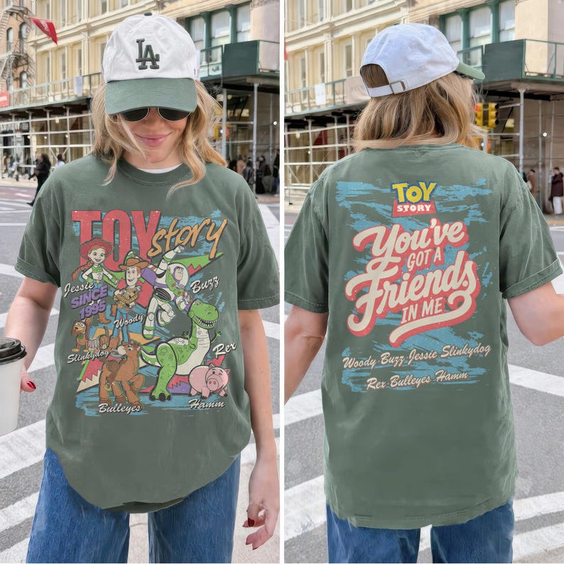 K&ouml;nnte beinhalten: Ein olivgr&uuml;nes T-Shirt mit Toy Story-Grafiken. Die Vorderseite zeigt Jessie, Woody, Buzz Lightyear, Slinky Dog, Bullseye, Rex und Hamm mit dem Text Toy Story Since 1995. Die R&uuml;ckseite zeigt den Text You've Got A Friends In Me.
