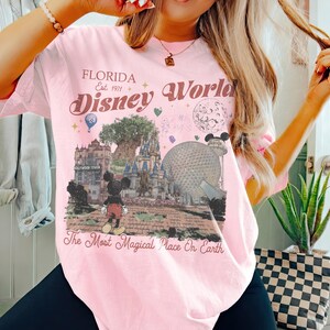 Puede incluir: Camiseta rosa claro con un gr&aacute;fico de Disney World. El gr&aacute;fico incluye el texto "Florida Est. 1971" y "Disney World" en una fuente vintage. El dise&ntilde;o presenta a Mickey Mouse, un castillo y el texto "The Most Magical Place On Earth."