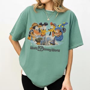 Pu&ograve; includere: T-shirt verde con una grafica dei personaggi Disney, tra cui Topolino, Paperino, Pippo e Pluto, e la scritta "Walt Disney World". La maglietta ha maniche corte e una vestibilit&agrave; rilassata.