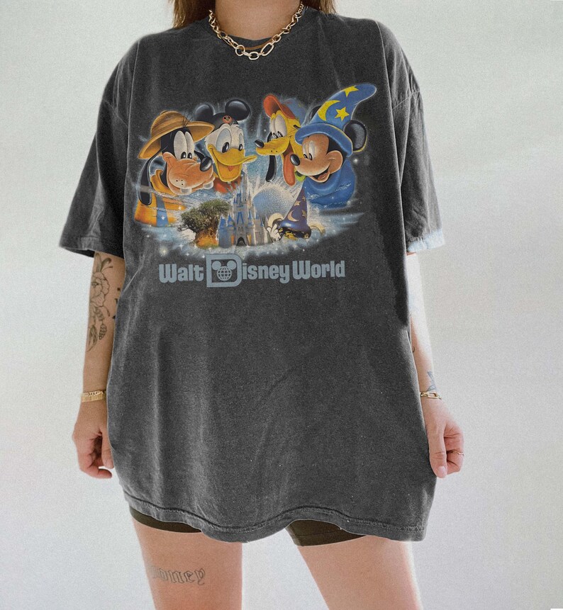 Pu&ograve; includere: T-shirt grigio scuro con una grafica dei personaggi Disney: Pippo, Paperino, Pluto e Topolino con un cappello da mago. Il testo "Walt Disney World" &egrave; stampato sotto. La maglietta ha maniche corte e una vestibilit&agrave; ampia.