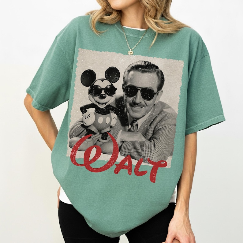 May include: A seafoam green t-shirt featuring a black and white image of Walt Disney and Mickey Mouse wearing sunglasses. The word "Walt" is printed in red script across the bottom of the image.