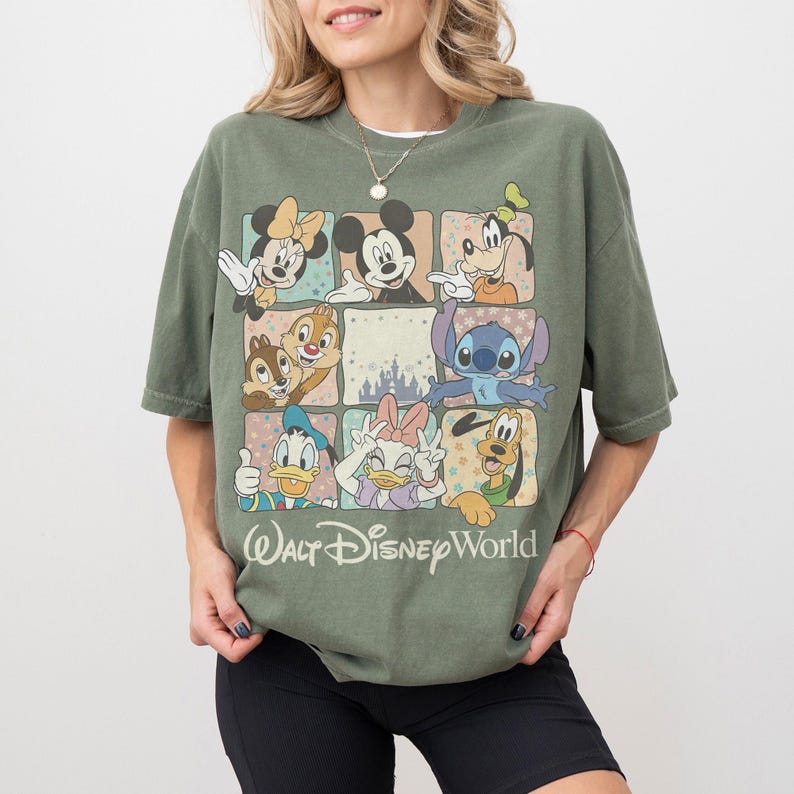 K&ouml;nnte beinhalten: Olivgr&uuml;nes T-Shirt mit einem Raster von Disney-Figuren, darunter Micky Maus, Minnie Maus, Goofy, Donald Duck, Daisy Duck, Chip und Chap und Stitch. Darunter steht "Walt Disney World".