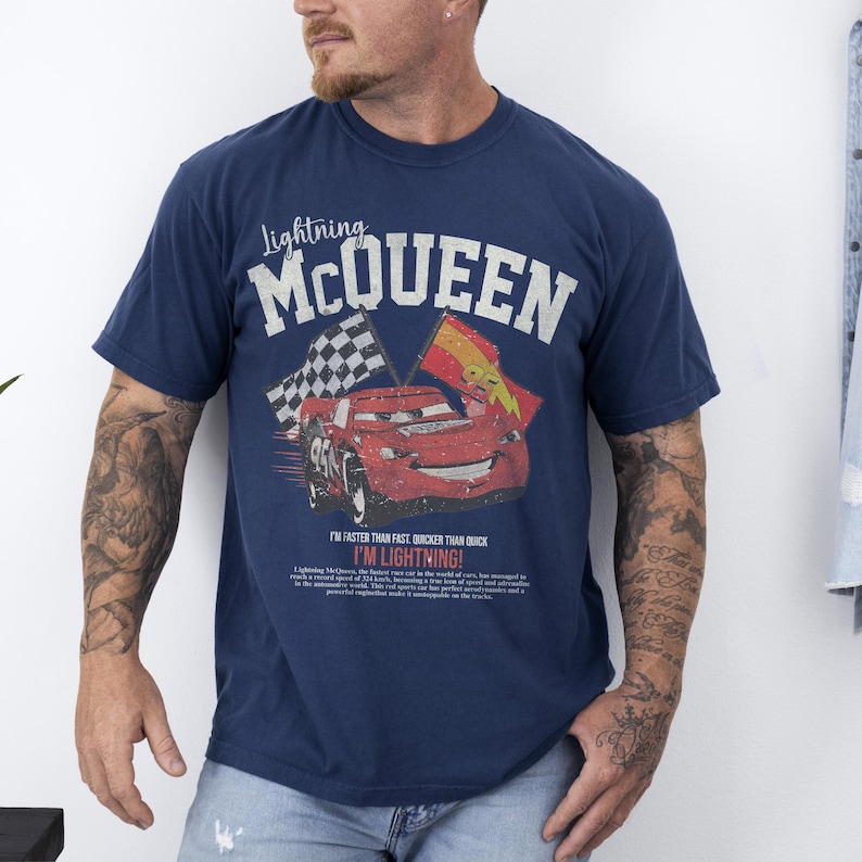 May include: Navy blue t-shirt featuring Lightning McQueen from the Cars movie. The graphic includes the text "Lightning McQueen" above a red race car with checkered and yellow flags. The text "I'M LIGHTNING!" is also visible.
