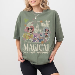 May include: Olive green t-shirt featuring a vintage-style graphic with Disney characters, including Mickey and Minnie Mouse, Donald Duck, and Goofy. The design includes the text "The Most Magical Place on Earth."
