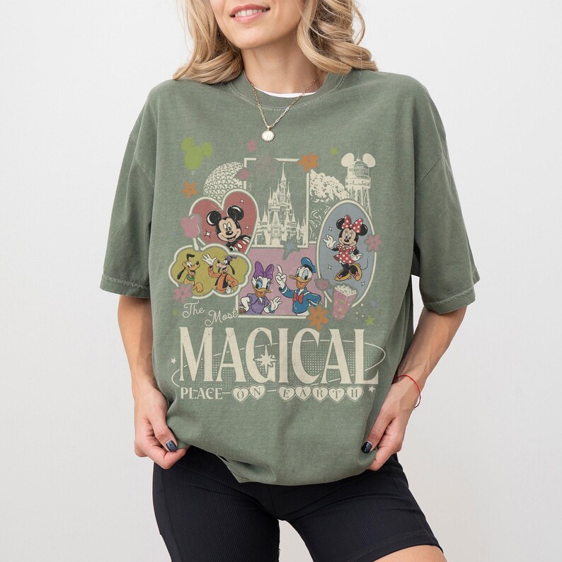 May include: Olive green t-shirt featuring a vintage-style graphic with Disney characters, including Mickey and Minnie Mouse, Donald Duck, and Goofy. The design includes the text "The Most Magical Place on Earth."
