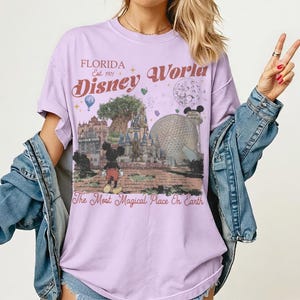 Puede incluir: Una camiseta de color lila con un gr&aacute;fico de Disney World. El dise&ntilde;o incluye a Mickey Mouse, un castillo y el texto "Florida Disney World Est. 1971" y "The Most Magical Place On Earth". La camiseta tiene mangas enrolladas.