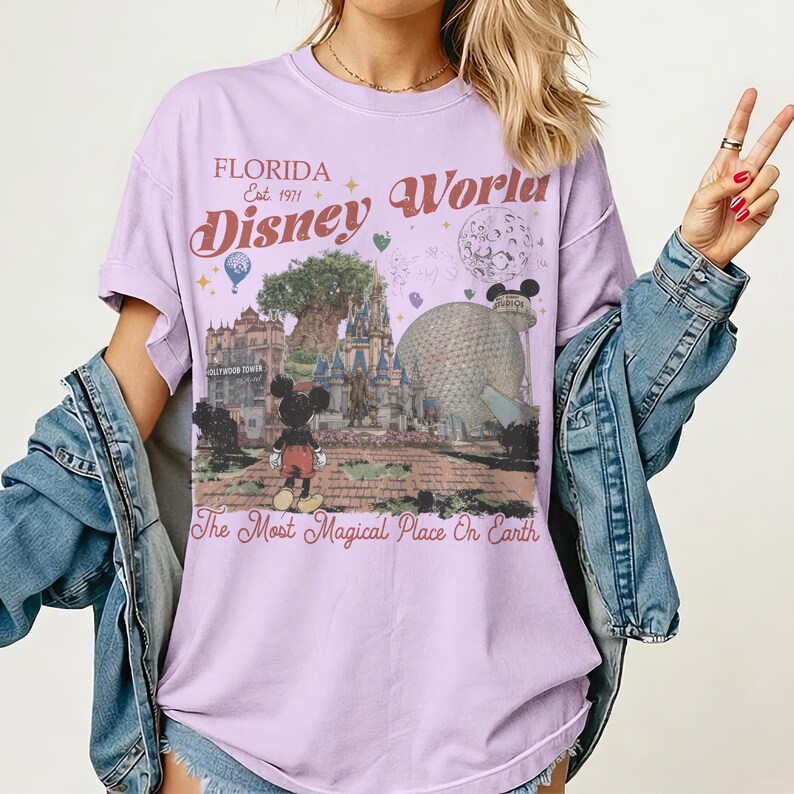 Puede incluir: Una camiseta de color lila con un gr&aacute;fico de Disney World. El dise&ntilde;o incluye a Mickey Mouse, un castillo y el texto "Florida Disney World Est. 1971" y "The Most Magical Place On Earth". La camiseta tiene mangas enrolladas.
