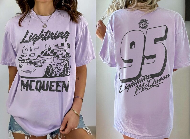 May include: Lavender t-shirt featuring a graphic of Lightning McQueen from the Cars movie. The front design includes the text "Lightning 95 McQueen" and a race car. The back displays a large "95" and "Lightning McQueen".