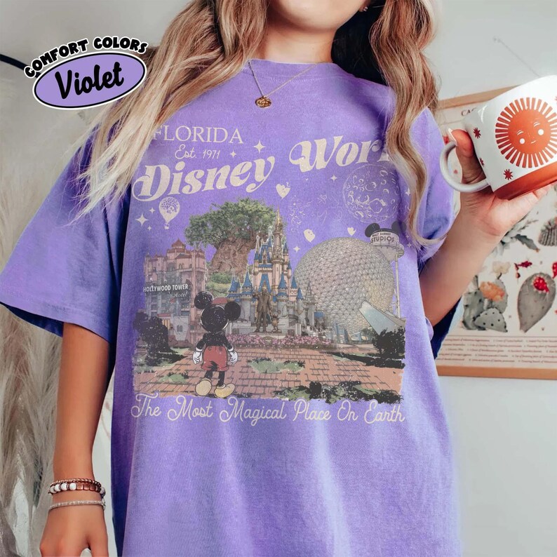 Puede incluir: Una camiseta violeta Comfort Colors con un gr&aacute;fico de Disney World. El dise&ntilde;o incluye el texto "FLORIDA Est. 1971 Disney World" y una imagen de Mickey Mouse, la Hollywood Tower y la bola de Epcot. La camiseta tambi&eacute;n tiene el texto "The Most Magical Place On Earth."