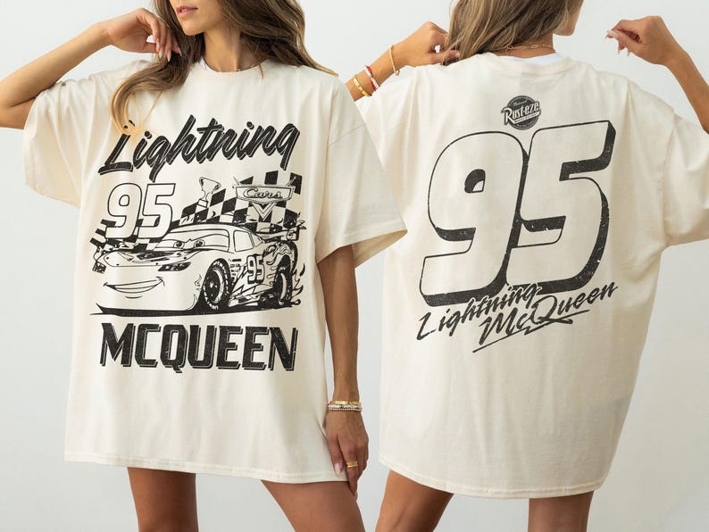 May include: Cream-colored t-shirt featuring a black graphic of Lightning McQueen race car with the number 95 and the name Lightning McQueen. The back of the shirt displays a large number 95 and the words Lightning McQueen.