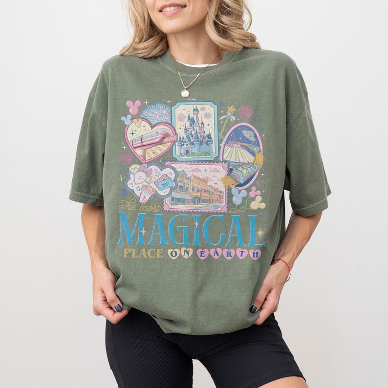 May include: Olive green t-shirt with a colorful graphic design. The design includes illustrations of a castle, a train, and other theme park elements. Text on the shirt reads "The most MAGICAL PLACE ON EARTH."
