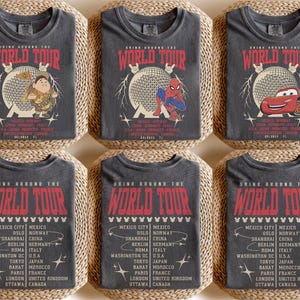 May include: Six gray t-shirts with the text "DRINK AROUND THE WORLD TOUR" in red. Each shirt features a different graphic: a cartoon character, Spider-Man, and a red race car. The shirts include a list of cities.