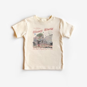 Puede incluir: Camiseta color crema con un gr&aacute;fico de Disney World de estilo vintage. El dise&ntilde;o incluye el texto "Florida Est. 1971 Disney World" y una ilustraci&oacute;n de Mickey Mouse y otros elementos del parque. La camiseta tiene mangas cortas y cuello redondo.