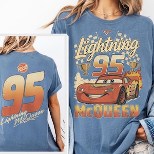 K&ouml;nnte beinhalten: Blaues T-Shirt mit Lightning McQueen aus dem Film Cars. Die Grafik auf der Vorderseite enth&auml;lt den Text "Lightning 95 McQueen" mit einem Cartoon-Bild des Autos und zwei Troph&auml;en. Auf der R&uuml;ckseite steht gro&szlig; "95" und der Text "Lightning McQueen".