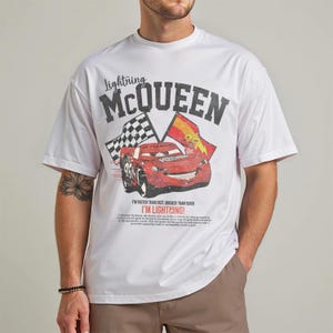 May include: White t-shirt featuring a graphic of Lightning McQueen from the Cars movie. The design includes the text "Lightning McQueen" above the car image, and "I'm faster than fast, quicker than quick, I'm Lightning!" below.