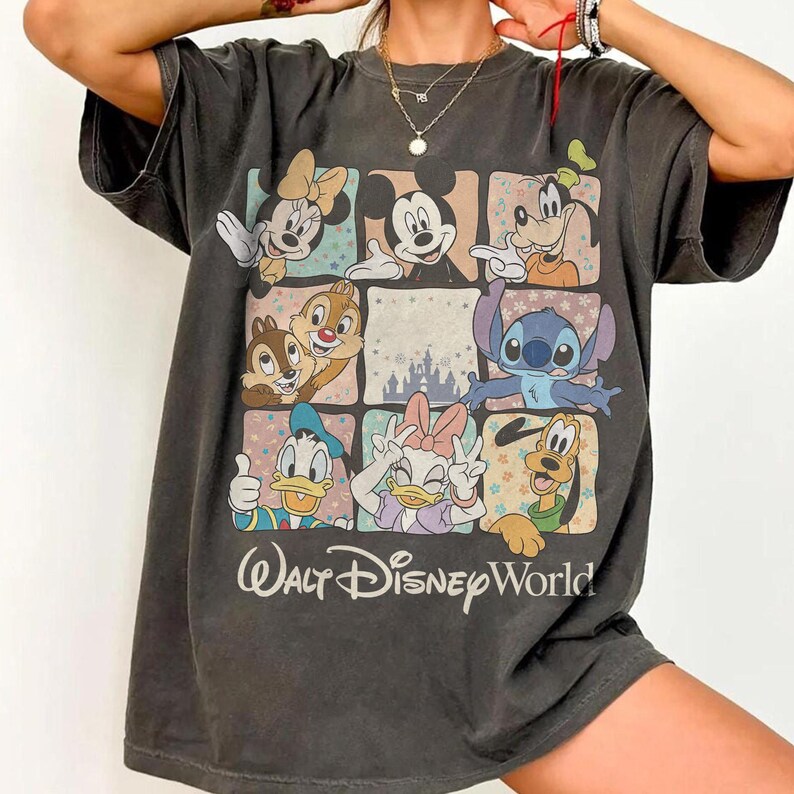 K&ouml;nnte beinhalten: Dunkelgraues T-Shirt mit einem Rastermuster, das Disney-Figuren wie Micky und Minnie Maus, Donald und Daisy Duck, Goofy und Stitch zeigt. Darunter steht "Walt Disney World".