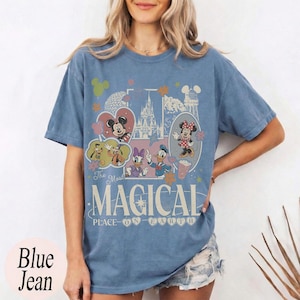 May include: Blue jean t-shirt featuring a colorful graphic with Mickey and Minnie Mouse, Donald and Daisy Duck, and other Disney characters. The shirt has the text "The Most Magical Place on Earth."