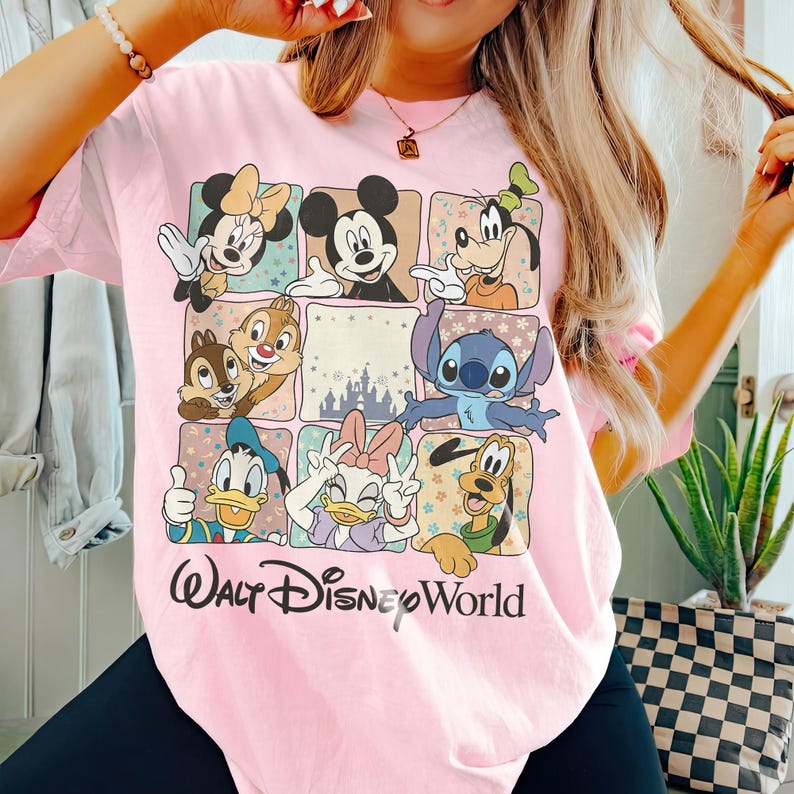 K&ouml;nnte beinhalten: Hellrosa T-Shirt mit einem Raster von Disney-Figuren, darunter Micky und Minnie Maus, Goofy, Donald und Daisy Duck, Chip und Chap und Stitch. Darunter steht in schwarzer Schrift "Walt Disney World".