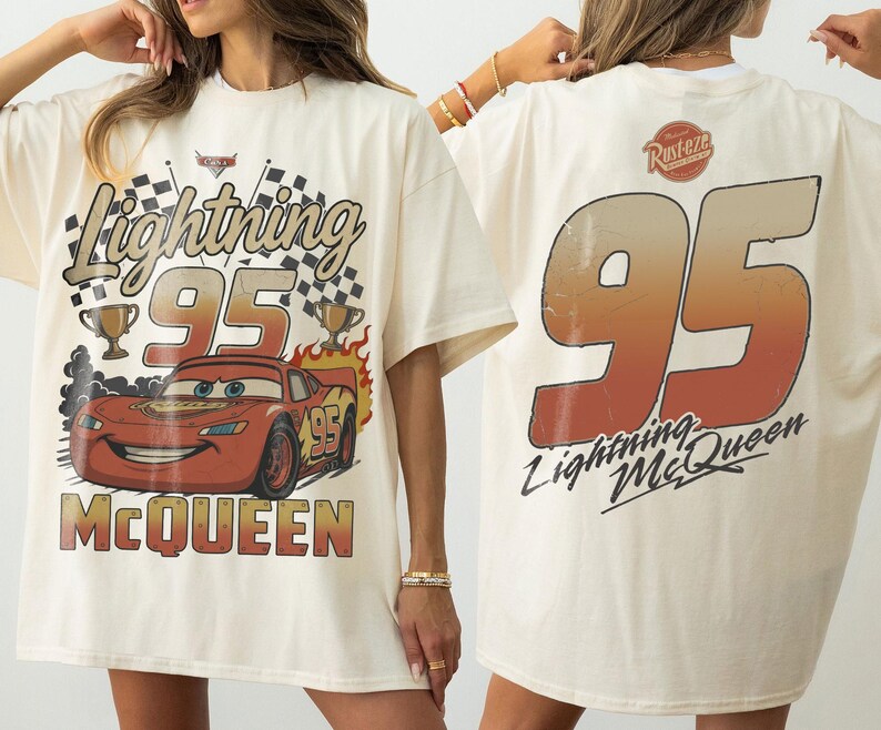 K&ouml;nnte beinhalten: Cremefarbenes T-Shirt mit einer Grafik von Lightning McQueen aus dem Film Cars. Auf der Vorderseite steht "Lightning 95 McQueen" mit Rennflaggen und Troph&auml;en. Auf der R&uuml;ckseite steht gro&szlig; "95" und der Text "Lightning McQueen".