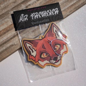 May include: A fox-shaped air freshener in a clear plastic bag with a black header card. The card features the text AIR FRESHENER, Honeysuckle, and FUJIWTR.COM. The air freshener has a stylized orange, red, and white fox face illustration.