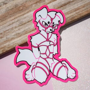 Peut inclure: Un autocollant découpé représentant un personnage canin anthropomorphe blanc avec des yeux et des marques noirs, attaché par une corde rose vif dans un motif de harnais complexe. Le personnage est à genoux et le contour est rose épais.
