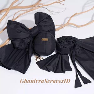 May include: A collection of black accessories, including a large bow, a round quilted purse with a gold-tone plaque, and a scarf. The accessories are arranged on a white surface with a few twigs in the background. The text "GhanirraScravesID" is at the bottom.