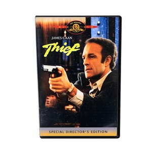 May include: A DVD case for the film Thief, featuring James Caan holding a handgun on the cover. The title Thief is printed in yellow text, with the MGM logo at the top and the text Special Director's Edition at the bottom of the black case.