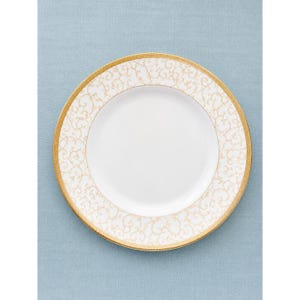May include: A round white porcelain dinner plate featuring a wide rim decorated with a delicate gold filigree scroll pattern. The center of the plate is plain white, and the outer edge is finished with a thin, solid gold band trim.