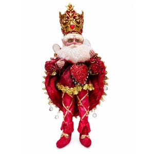 May include: A decorative figurine of a figure wearing a gold crown with red accents, a white beard, and red clothing. The outfit features a large red heart on the chest, gold sequin trim, and red leggings with gold crisscross patterns and red boots.