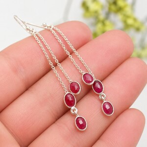 May include: A pair of long drop earrings featuring silver chains and multiple faceted oval-shaped red gemstones. Each earring consists of a delicate silver chain suspending two or three small, polished red stones in secure metal settings.
