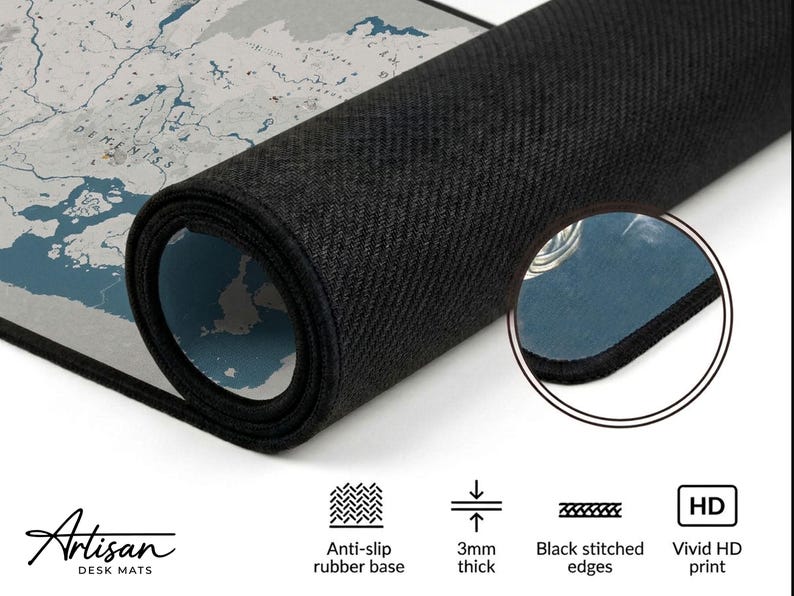 Puede incluir: Alfombrilla de escritorio enrollada con un dise&ntilde;o de mapa del mundo en tonos grises y azules. La alfombrilla tiene una base de goma antideslizante negra, bordes cosidos negros y tiene 3 mm de grosor. El texto "Artisan DESK MATS" es visible.
