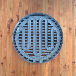 May include: A circular gray metal grill grate featuring a prominent, raised, serpentine-shaped heating element pattern centered within a grid of horizontal and vertical bars, designed for use as a replacement component for a cooking appliance.