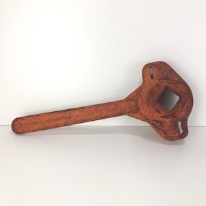 May include: A rusty orange metal wrench with a square socket and a long handle. The handle is embossed with the text "ROCKWELL MANUFACTURING". The tool has a vintage appearance and is likely made of steel.