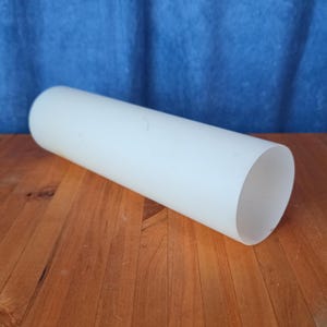 May include: A cylindrical, opaque white object with rounded ends. The object is lying on a wooden surface, with a blue background. The object appears to be made of a solid material.