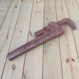 May include: A heavy-duty pipe wrench with a rusted, dark brown metal finish. The tool features a long handle, an adjustable jaw mechanism with visible teeth, and the number 18 stamped clearly into the metal near the base of the handle.