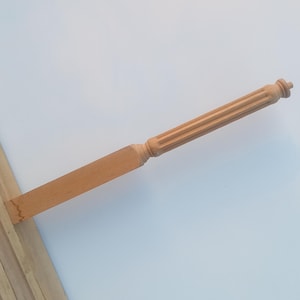 May include: A light brown wooden furniture leg with a fluted column design and a rectangular base. The leg is angled, showing the detailed craftsmanship of the wood. The overall design is classic and elegant.