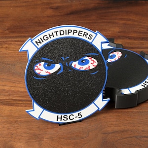 May include: A circular black patch featuring a graphic of two bloodshot blue eyes centered on a dark background. The design includes a white banner at the top with the text NIGHTDIPPERS and a white banner at the bottom with the text HSC-5.