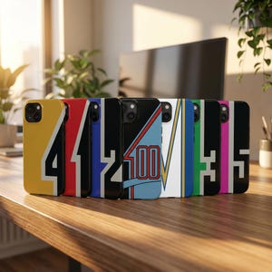 May include: A collection of phone cases with various designs and colors. Each case features a different number or graphic, including the numbers "4", "41", "2", "100", and "5". The cases are displayed on a wooden surface.