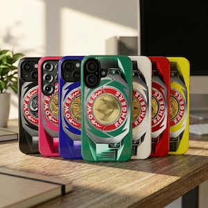 May include: A row of colorful phone cases featuring a Power Rangers design. The cases are black, pink, blue, green, white, red, and yellow. Each case has a gold emblem with the words "Power Rangers" around the edge.