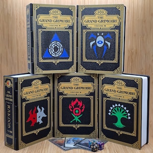 May include: A collection of five black storage boxes designed to look like antique books, each labeled "The Grand Grimoire Volume II." The boxes feature gold trim and unique emblem designs in blue, red, and green. The spine of one box reads "RAKDOS."
