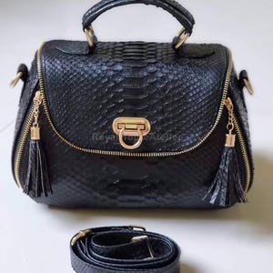 Peut inclure: Sac à main noir avec un motif en peau de serpent texturé, doté d'une poignée supérieure et d'une bandoulière amovible. Le sac a des fermetures éclair et des accessoires dorés, avec des glands sur les tirettes. Le sac est de forme carrée.